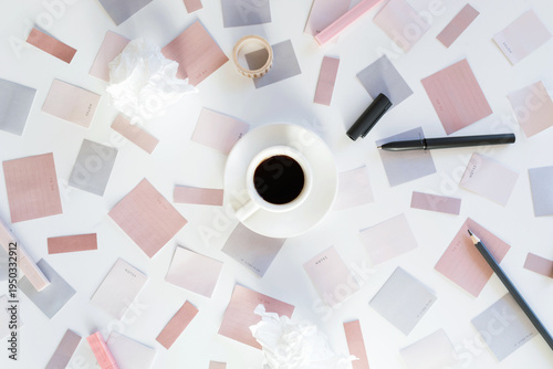 Overhead view of a coffee cup surrounded by a creative mess of colorful sticky notes, pens, and crumpled paper representing a brainstorming process in a home office.
