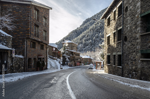 A winter morning in a picturesque mountain village, where traditional stone buildings line a gently curving road dusted with fresh snow. 
