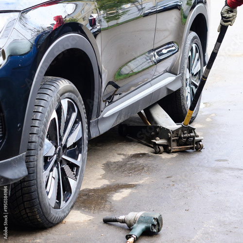 Car is being lifted with a jack for maintenance tasks on a concrete surface in a garage during daylight hours