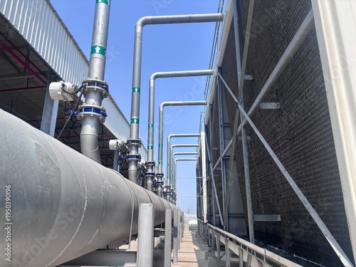 Fotografi Detailed outdoor view of a large-scale industrial cooling tower system featuring long metallic pipelines with green flow direction arrows