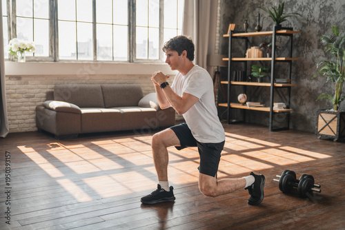 Active Caucasian man doing forward lunges during fitness workout at home. Young athletic sportsman training legs in living room. Healthy lifestyle and body care concept.