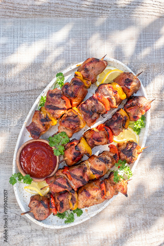 Delicious grilled kebabs with peppers and lemon slices served on a platter with sauce