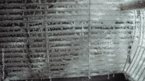 Frostcovered reactor grate interior, icy metal ribs and sootstained slats show nuclear winter aftermath, drone inspection perspective reveals layered frost, rust, and sediment on industrial vent,