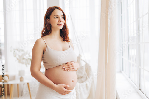 Smiling pregnant woman touching belly in bright minimal home interior near window Free Download Smiling pregnant woman touching belly in bright minimal home interior near window - GFXLoad