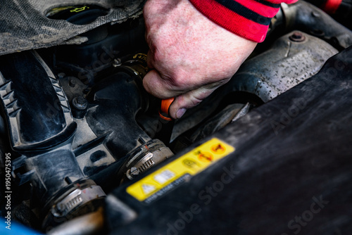 A mechanic holding an oil level gauge in one hand is checking the car's oil level for maintenance.