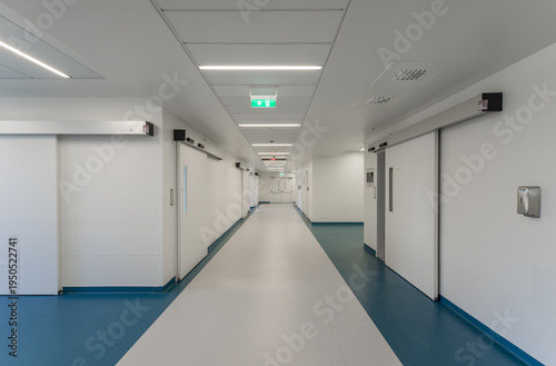 Modern hospital corridor interior with elevators and emergency exit signs.