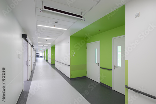 Modern hospital corridor interior with elevators and emergency exit signs.