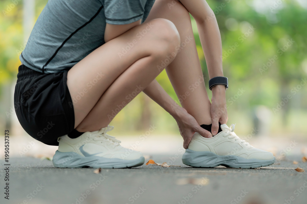 Obraz premium Young woman suffering ankle pain after running in park, squatting and holding injured foot, sports injury and sprained ankle outdoor fitness concept. workout, foot, sprain, strain, ankle, pain, injury
