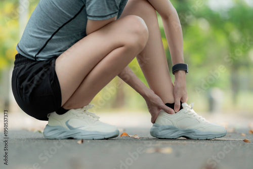 Young woman suffering ankle pain after running in park, squatting and holding injured foot, sports injury and sprained ankle outdoor fitness concept. workout, foot, sprain, strain, ankle, pain, injury