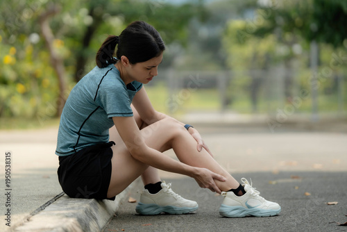 Young woman sitting on curb with leg pain after running in park, holding sore shin muscle, sports injury and overuse strain outdoor fitness concept. workout, park, muscle, strain, , injury, shin, leg