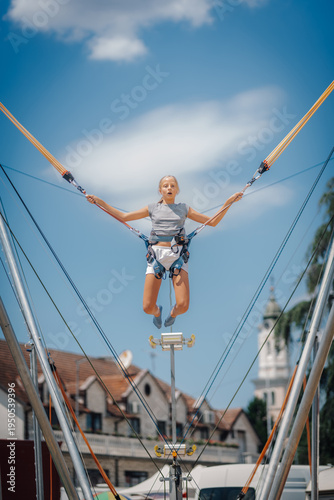 Obraz na plátně Teenage girl jumping on bungee trampoline having fun in city center during summe