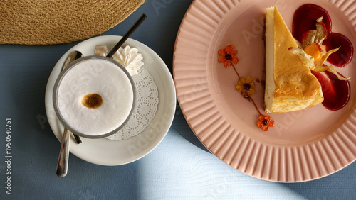 Top view of cheesecake with berry sauce and a cappuccino on a blue table. Flat lay composition with natural sunlight and shadow.
