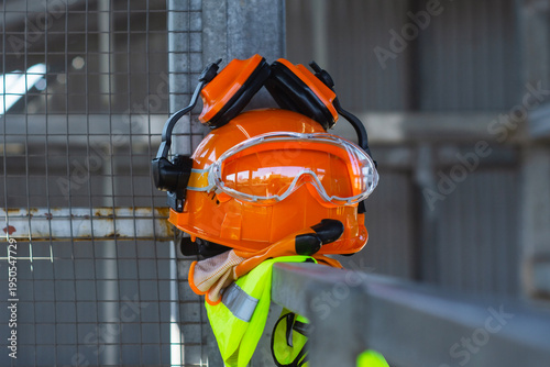 Construction safety helmet with protective goggles, ear protection and work gloves at building site. Personal protective equipment for industrial work, construction safety and workplace protection.