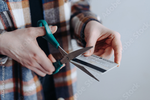 woman hands cutting grey plastic bank credit card with black stripe with scissors, young caucasian woman in warm plaid shirt, banking services concept, selective focus, close-up view of hands