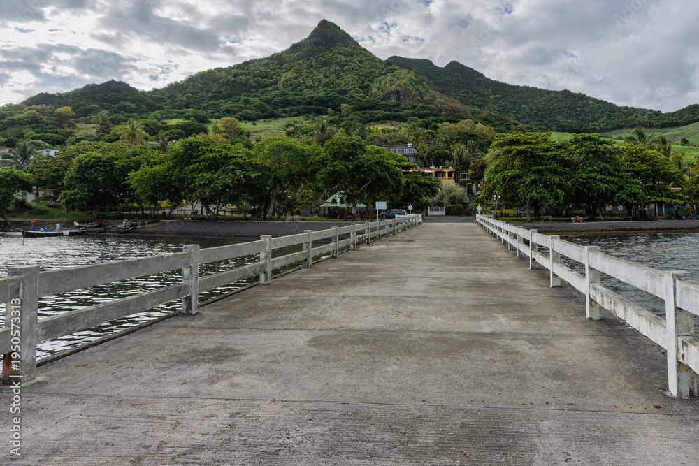 Fototapeta premium Long concrete pier stretching toward a lush green mountain landscape in a tropical coastal setting at Bois des Amourettes, Mauritius island
