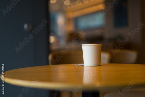 Fotografía A white paper cup placed on a wooden round table in a softly lit indoor setting