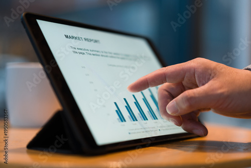 A man's finger touches a tablet screen displaying market report charts and data visualization