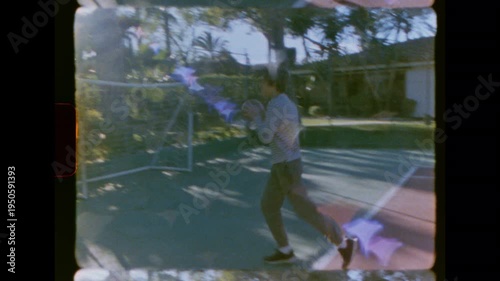 Authentic vintage 8mm film footage of a young man dribbling a basketball on a residential court. He moves across the court on a sunny day. The camera tilts up to the hoop. Nostalgic and retro feel.