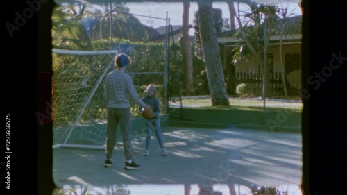 Vintage 8mm film captures a boy and girl playing basketball on a backyard court. Authentic home movie footage shows siblings having fun together on a sunny day. Nostalgic family moments.