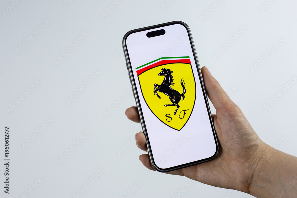 Fototapeta premium Moscow, Russia, March 14, 2026: Hand holding smartphone displaying Scuderia Ferrari shield logo with prancing horse and SF letters on screen. Legendary racing team heritage and motorsport tradition