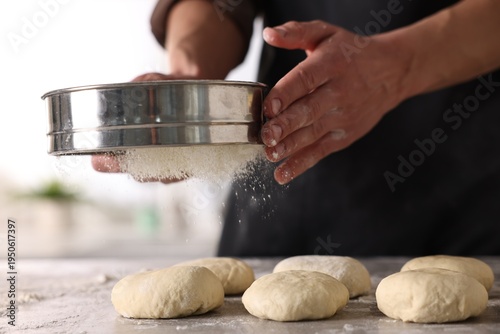 Obraz na plátně Man sifting flour onto dough at grey table indoors, closeup