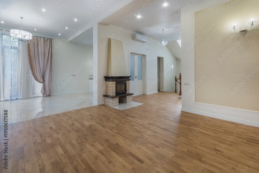 Obraz premium A bright living area has a wooden floor and large windows. The room features a fireplace and an open layout leading to other spaces. Curtains are present on one side