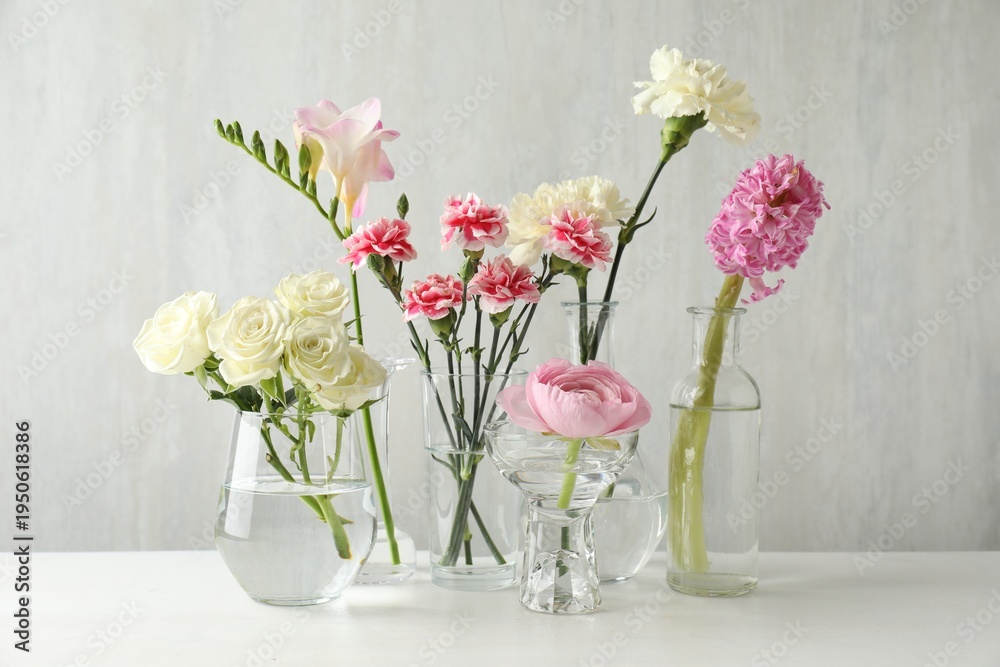 Fototapeta premium Different beautiful flowers in vases on light table indoors