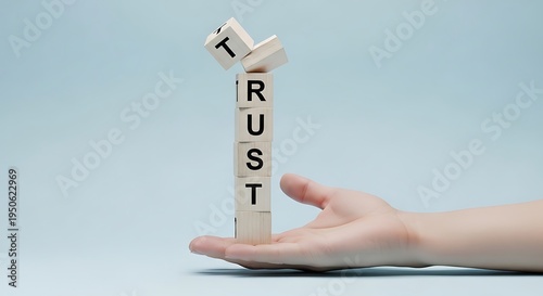 A human hand holding a precarious stack of wooden blocks spelling out the word trust on blue background