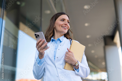 Female doctor walking outdoors while holding phone and notebook