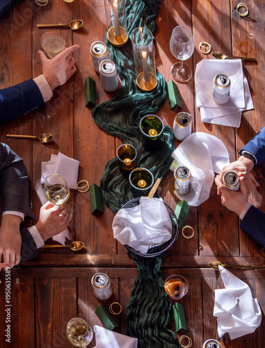 High angle detail shot of a table at a formal reception with glasses, candles, and beer with hands.