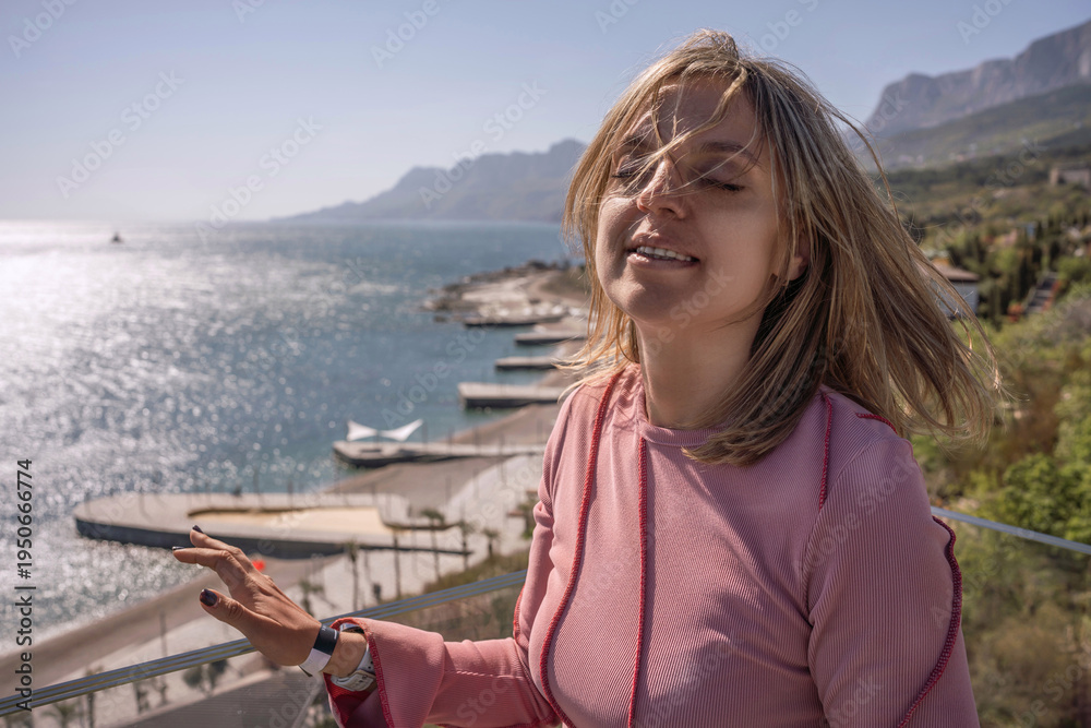 Fototapeta premium Woman vacation seaside beautiful blonde female traveler enjoys warm wind and sunshine overlooking blue ocean