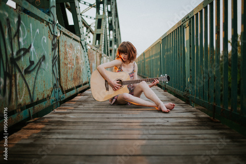 Young Woman with Acoustic Guitar Sitting on Industrial Bridge