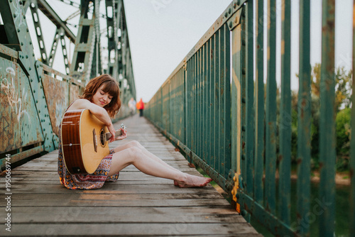 Young Woman Sitting Barefoot on Bridge Playing Acoustic Guitar