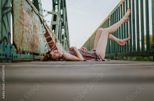 Young Woman Lying on Wooden Bridge with Acoustic Guitar