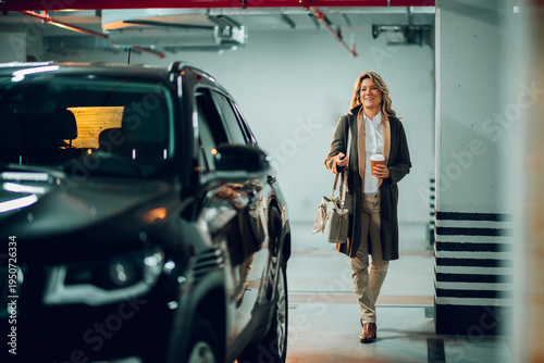 Professional businesswoman walking toward her vehicle in a dimly lit underground parking lot, carrying a handbag and takeaway coffee