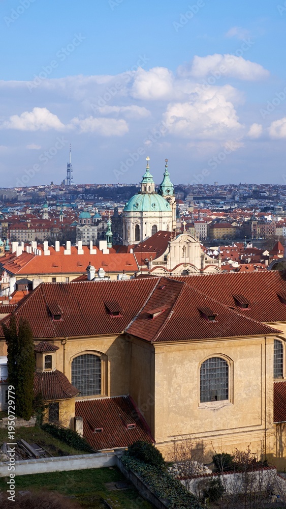 Obraz premium St Nicholas Church crowns Prague skyline above red tile rooftops under blue sky