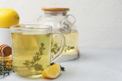 Fresh thyme tea in glass cup and slice of lemon on grey table, closeup. Space for text