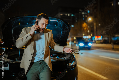 Canvas Print Man talking on phone, car hood open at night, experiencing breakdown and calling