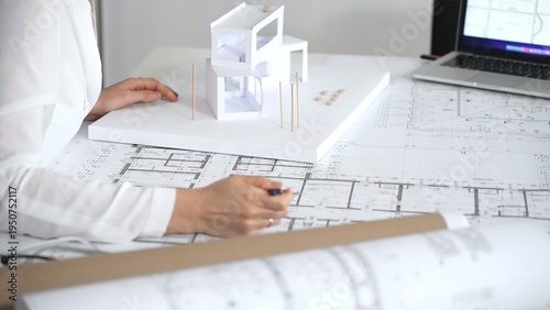 Obraz na plátne Female architect engrossed in architectural plans and miniature scale model, tho