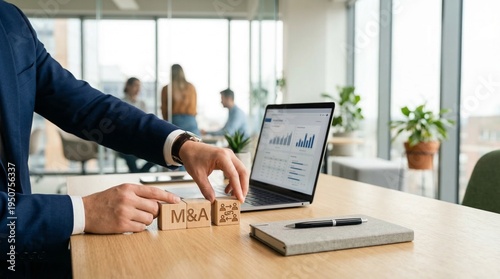 Business Merger and Acquisition Concept: An executive in a modern office sets up wooden blocks spelling out M&A symbolizing the concept of business merger and acquisition.