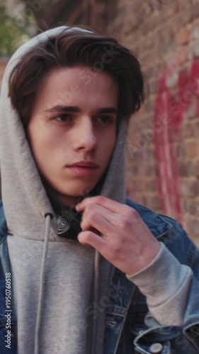 Serene adolescent portrayed in city environment sporting mask and relaxed casual attire contrasted by brick wall