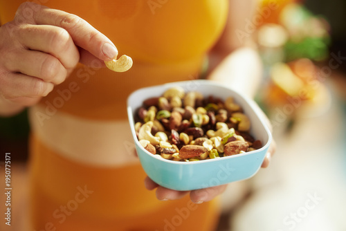 Close-up of a person in an orange striped shirt picking a cashew from a blue bowl of mixed nuts and fruit, highlighting mindful snacking and nutritious food choices.
