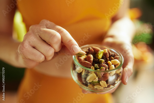 Detail of a person selecting a pistachio from a glass bowl of mixed nuts, focusing on healthy snack choices and weight management through mindful nutrition.
