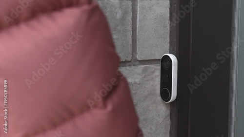 Person in brown puffer jacket approaches a doorbell camera mounted on a stone wall, preparing to interact with the device at the entrance