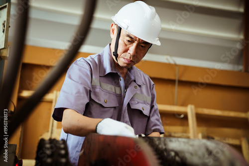 Senior Asian engineer inspecting machinery in factory.