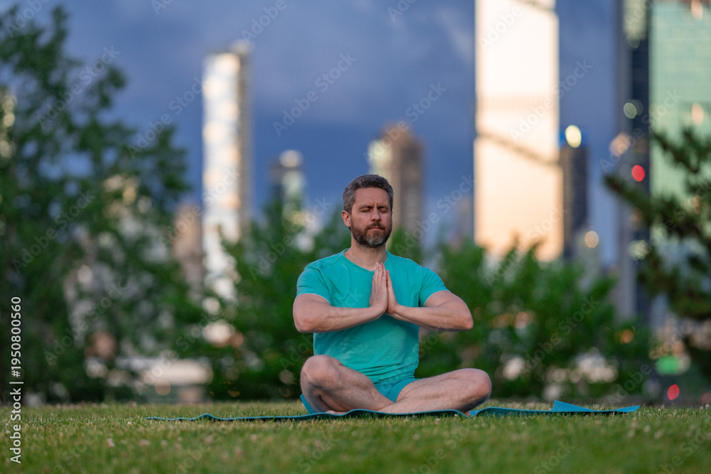 Fototapeta premium Man meditating with peaceful expression. Man practicing yoga outdoors in nature. Man sitting in lotus meditation pose. Man enjoying calm wellness moment.