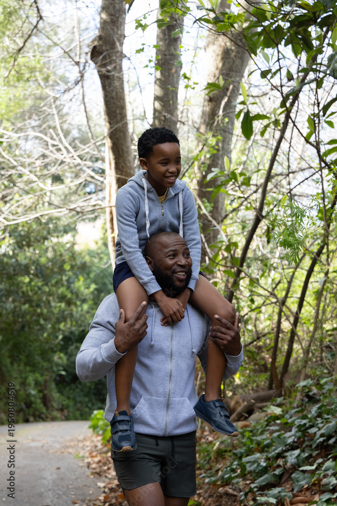 Naklejka premium African American father and child walking on paved trail, child riding on shoulders, zip-up hoodies