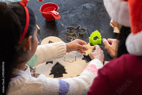 Parent and child cutting cookies on dark kitchen countertop, holding star dough, wearing Santa hat