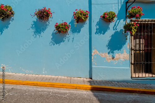 Frontal view of vibrant blue house facade with hanging flower pots casting shadows on weathered wall in historic city street
