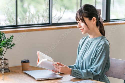 фотографія A young Asian woman reading a book (self-help) in a cafe.